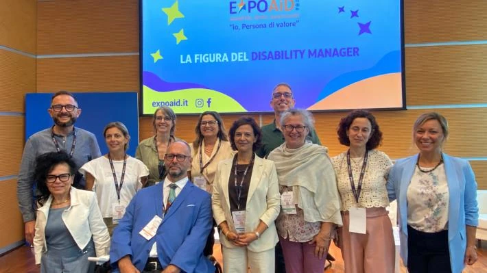Palma Marino Aimone in una foto di gruppo all’ExpoAID, davanti allo schermo «La figura del Disability Manager».